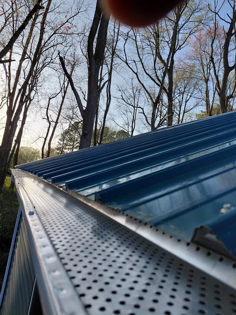 Blue metal roof gutters with perforated surface against bare trees and blue sky