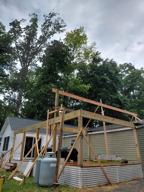 Wooden frame structure under construction attached to a beige house with lattice foundation skirting