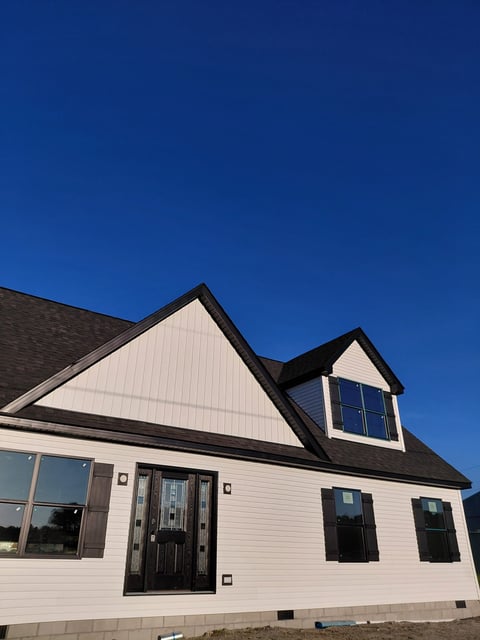 Modern white house with black roof and dormers against clear blue sky