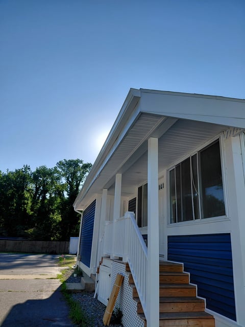 Modern white house with blue accents, covered porch with white columns, and wooden steps under clear blue sky
