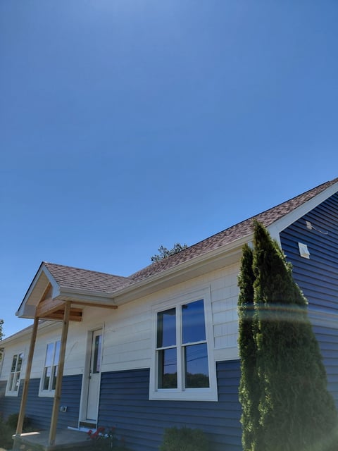 Modern residential home with blue and white exterior, large windows, gabled roof, and climbing ivy under clear blue sky