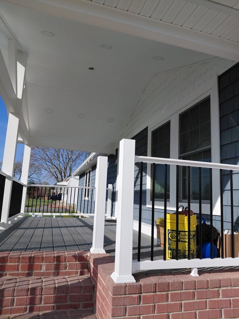 Modern house front porch with white columns, black-framed windows, brick foundation, and covered deck under white ceiling