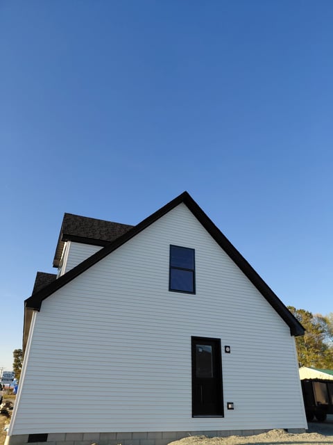 Modern white house with black roof and trim, featuring one upper window and one lower door, set against clear blue sky