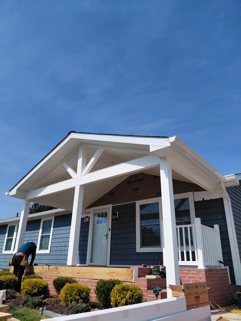 Modern blue and white cottage with brick foundation, covered porch, and clear blue sky above