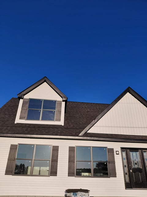 Modern two-story house with white siding, dark roof, multiple windows with shutters, and garage against clear blue sky